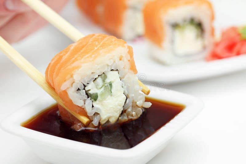 Sushi roll in chopsticks in soy sauce