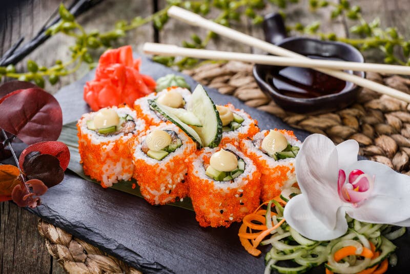 Sushi Roll - Maki Sushi made of Salmon, Red caviar, cucumber. Avocado and cream cheese on black stone on bamboo mat decorated with flowers. Japanese cuisine royalty free stock images Sushi Roll - Maki Sushi made of Salmon, Red caviar, cucumber. Avocado and cream cheese on black stone on bamboo mat decorated with flowers. Japanese cuisine royalty free stock images