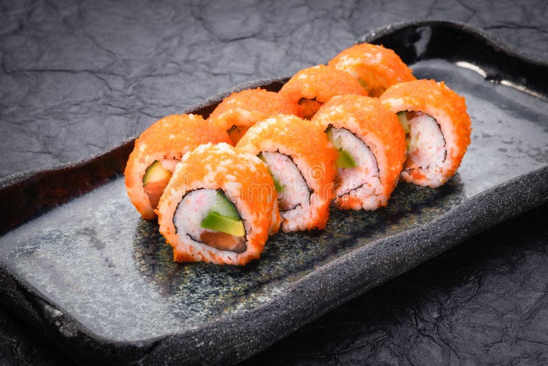 Sushi set served on dark background. Maki roll, Philadelphia maki with masago, salmon, cream cheese, avocado and prawn