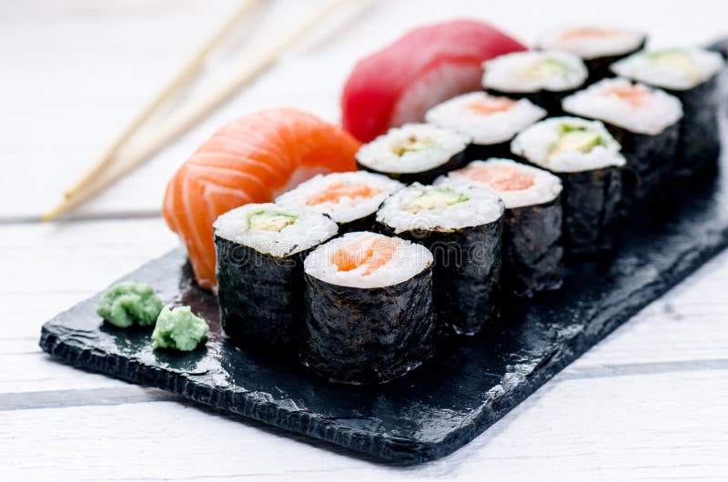 Sushireeks op een zwarte lei wordt gediend die Sushibroodjes en sashimi op een houten witte lijst Zeevruchten Ruwe Vissen Witte a stock fotografie Sushireeks op een zwarte lei wordt gediend die Sushibroodjes en sashimi op een houten witte lijst Zeevruchten Ruwe Vissen Witte a stock fotografie