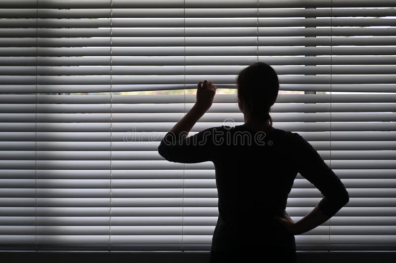 Suspicious woman looking outside through a venetian curtain blinds