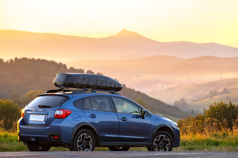 SUV car with roof rack luggage container for off road travelling parked at roadside at sunset. Road trip and getaway concept