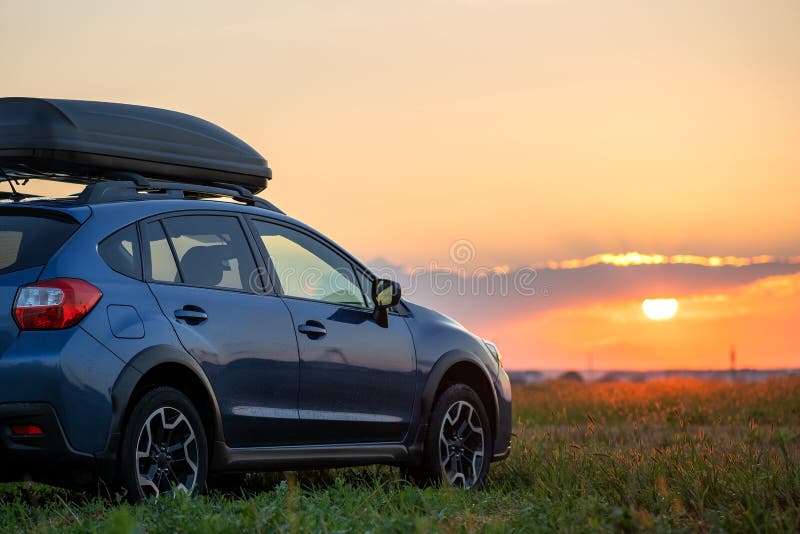 SUV car with roof rack luggage container for off road travelling parked at roadside at sunset. Road trip and getaway concept