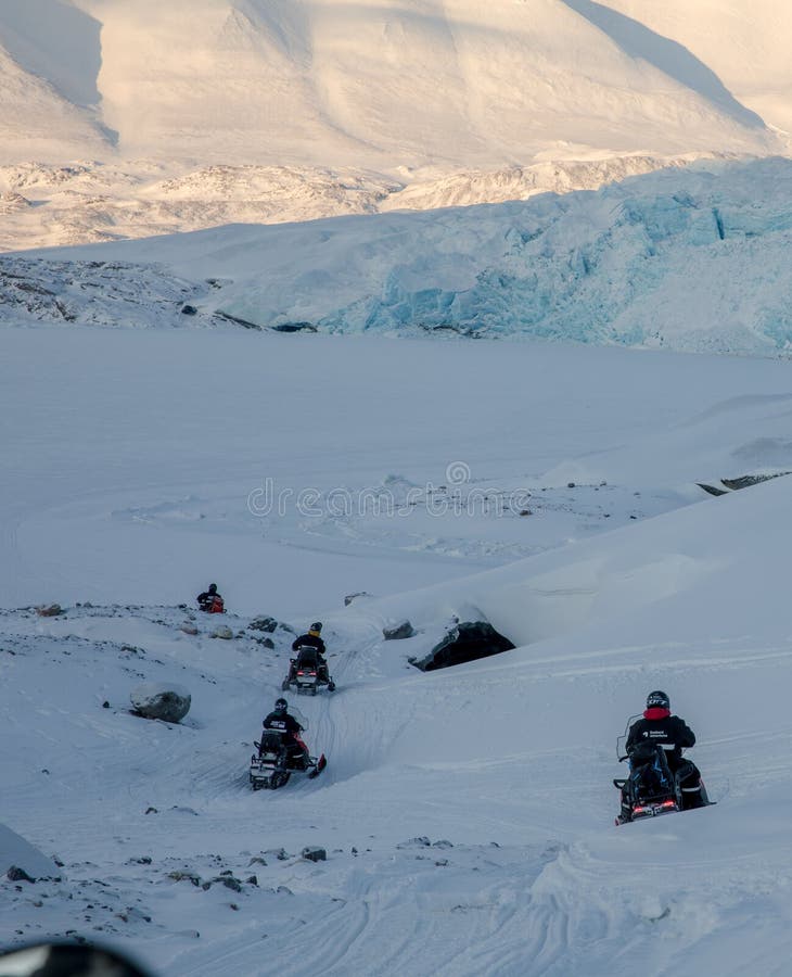 Svalbard, Norway - march 2019: Four snowmobiles driving downhill through the arctic winter landscape in Svalbard, Norway
