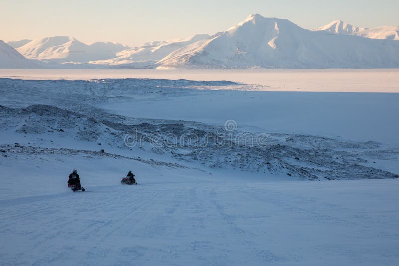 Svalbard, Norway - march 2019: Two snowmobiles driving through the arctic winter landscape in Svalbard, Norway