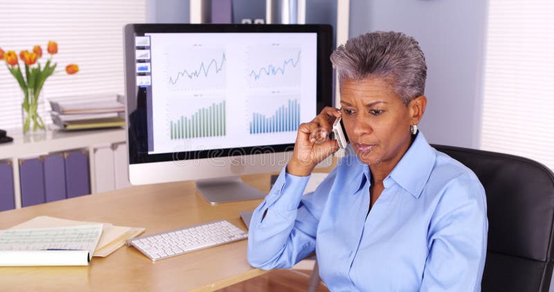 Svart affärskvinna för pensionär som talar på telefonen vid datoren