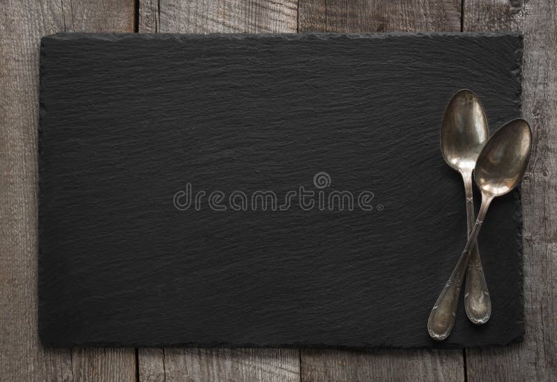 Black slate plate and vintage spoons on wooden board. Top view. Space for your text. Black slate plate and vintage spoons on wooden board. Top view. Space for your text.