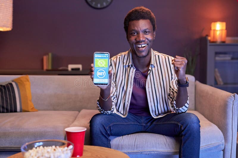 Portrait of excited black man watching sports match on TV at home and using online betting app in blue light, copy space. Portrait of excited black man watching sports match on TV at home and using online betting app in blue light, copy space