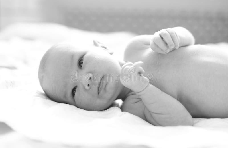 Black and white portrait of little smiling newborn baby lying sidelong in baby bed at home. Little cute baby, closeup. Black and white portrait of little smiling newborn baby lying sidelong in baby bed at home. Little cute baby, closeup