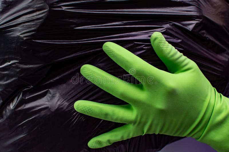 Svart plastpåsstruktur i händerna i grön handskar bakgrund Abstrakt illustration av rengöring och sortering av skräp royaltyfri bild