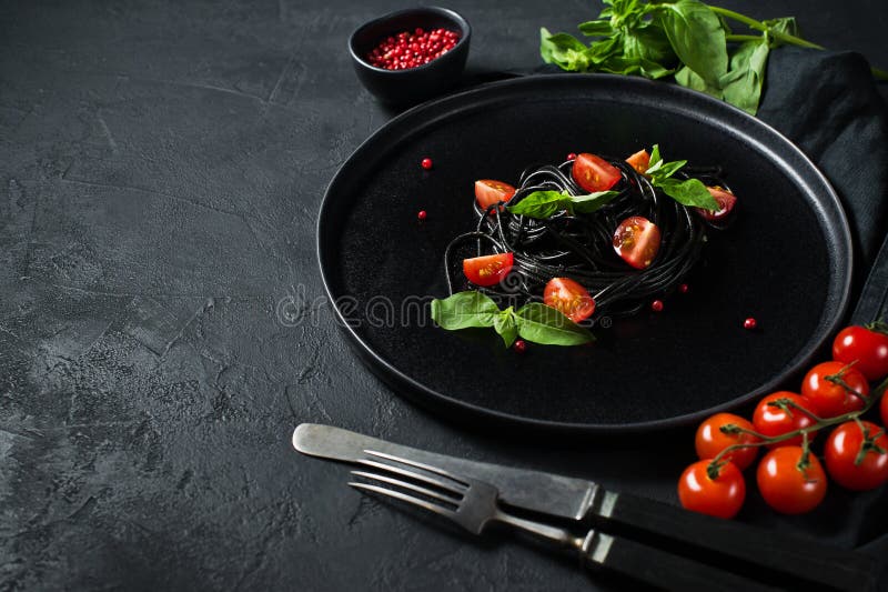 Svart spagetti med basilika och k?rsb?rsr?da tomater, vegetarisk pasta Svart bakgrund, b?sta sikt, utrymme f?r text arkivfoto Svart spagetti med basilika och k?rsb?rsr?da tomater, vegetarisk pasta Svart bakgrund, b?sta sikt, utrymme f?r text arkivfoto