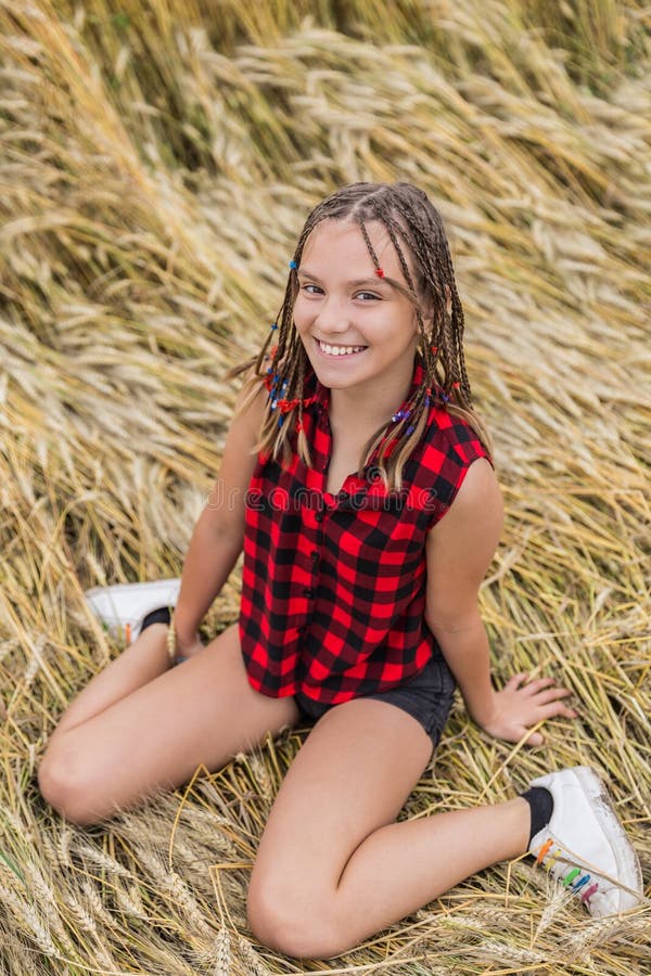 Sväng tonårsflicka med braider som sitter i vetefält på sommaren fotografering för bildbyråer