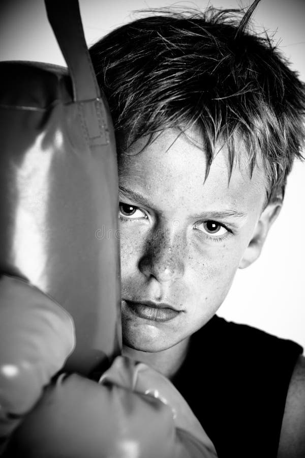 Sweating child wearing boxing gloves and dark sleeveless shirt leaning against punching pad in black and white. Sweating child wearing boxing gloves and dark sleeveless shirt leaning against punching pad in black and white