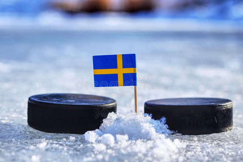 Švédská vlajka na párátku mezi dvěma hokejovými puky. Švédsko bude hrát na mistrovství světa ve skupině B. 2019 IIHF World Championship