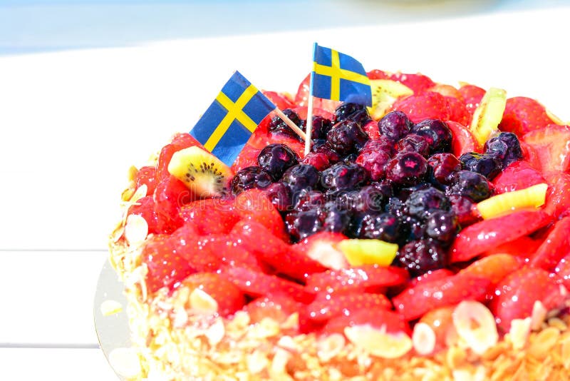 Swedish summer cake with cream, strawberries and fruit, garnished almonds around in thin slices. sun and copy space and swedish flags its midsummer. Swedish summer cake with cream, strawberries and fruit, garnished almonds around in thin slices. sun and copy space and swedish flags its midsummer