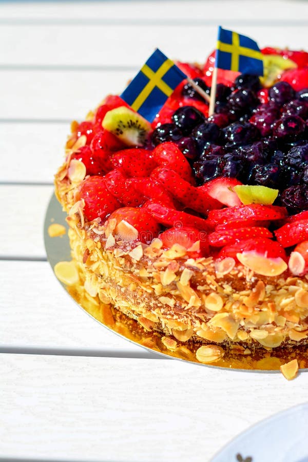 Swedish summer cake with cream, strawberries and fruit, garnished almonds around in thin slices. sun and copy space and swedish flags. Swedish summer cake with cream, strawberries and fruit, garnished almonds around in thin slices. sun and copy space and swedish flags