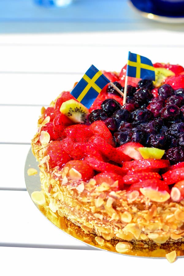 Swedish summer cake with cream, strawberries and fruit, garnished almonds around in thin slices. sun and copy space and swedish flags. Swedish summer cake with cream, strawberries and fruit, garnished almonds around in thin slices. sun and copy space and swedish flags