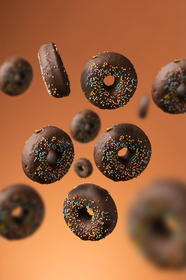 Sweet chocolate donuts with multicolored sugar sprinkles on an orange background. Desser in motion and levitation.