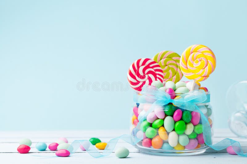 Sweet colorful candy in jar decorated with bow ribbon against blue background. Gifts for Birthday party.