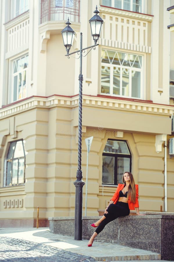 A sweet face is a mystery. Fashion portrait of a happy woman in red style jacket and black pants sits on the background of new hou stock photo A sweet face is a mystery. Fashion portrait of a happy woman in red style jacket and black pants sits on the background of new hou stock photo