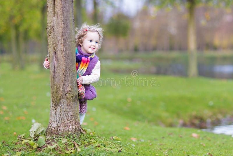 Sweet funny toddler girl hiding behind a tree in a beautiful autumn park. Sweet funny toddler girl hiding behind a tree in a beautiful autumn park