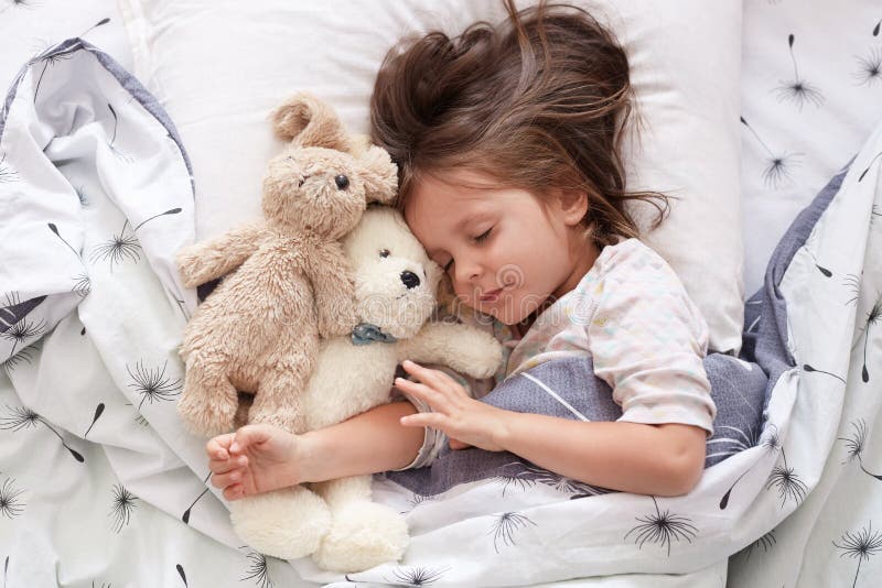 Sweet little girl sleeping with toys in crib. Close up portrait of infant sleeping in cot. Beautiful toddler sleeping with toy