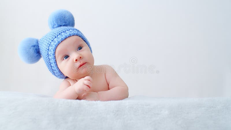 Sweet Newborn Baby in a Blue Hat with Pompoms Looks into the