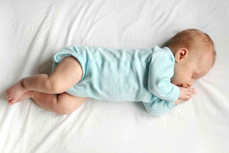A precious newborn infant is laying on a comfortable white bed, sleeping peacefully. A precious newborn infant is laying on a comfortable white bed, sleeping peacefully.