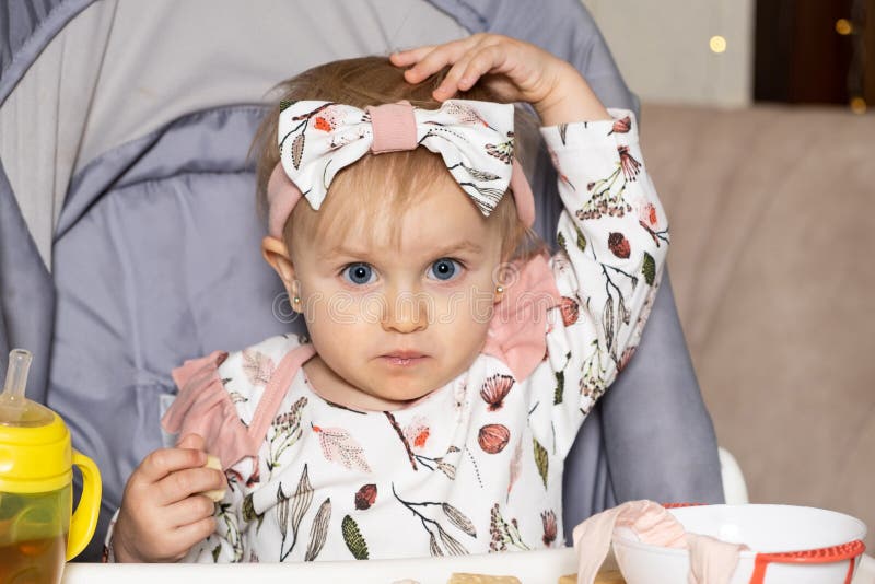 A Sweet One and a half year old Girl Sits In A High Baby Feeding Chair a-sweet-one-and-a-half-year-old-girl-sits-in-a-high-baby-feeding-chair
