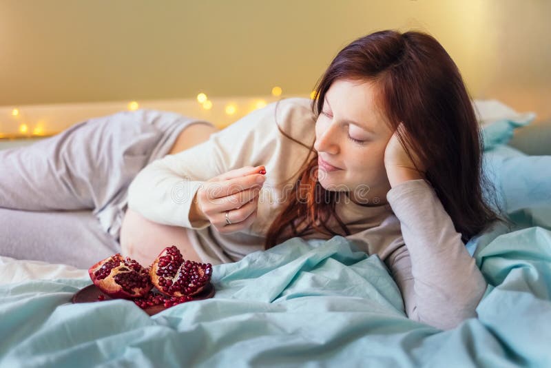 Happy pregnant woman resting on bed,eating pomegranate