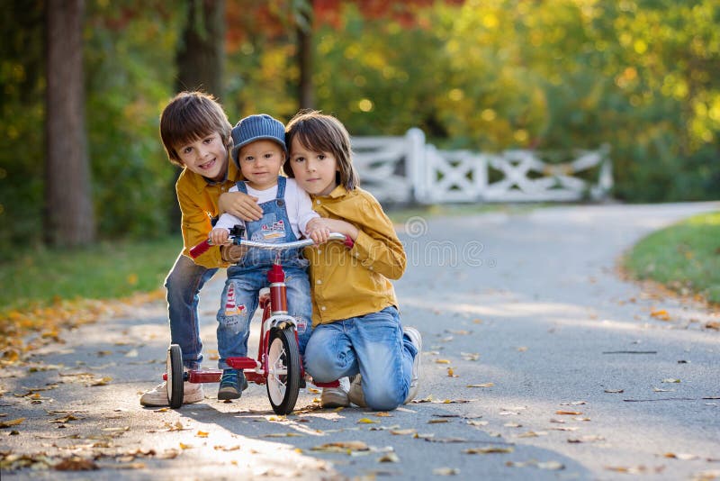 Sweet toddler boy, riding tricycle in the park on sunset, autumn time, siblings in the park, enjoying warn autumn day