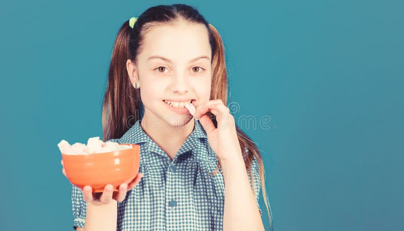 Sweet tooth concept. Calorie and diet. Girl smiling face hold bowl sweet marshmallows in hand blue background. Kid girl royalty free stock photo Sweet tooth concept. Calorie and diet. Girl smiling face hold bowl sweet marshmallows in hand blue background. Kid girl royalty free stock photo