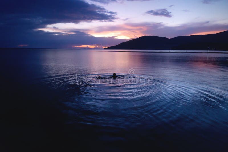 Swimming person at orange sunset on purple blue sky along lake Itza, El Remate, Peten, Guatemala