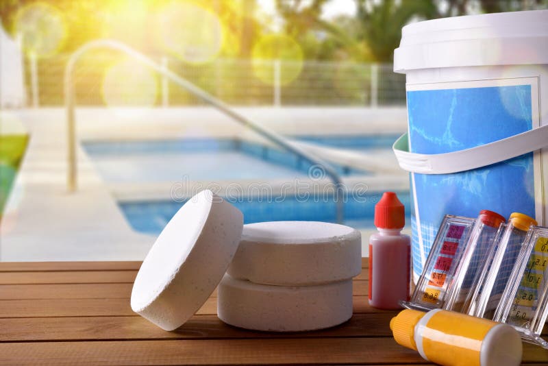 Swimming pool service and equipment with chemical cleaning products and tools on wood table and pool background. Horizontal composition. Front view. Swimming pool service and equipment with chemical cleaning products and tools on wood table and pool background. Horizontal composition. Front view