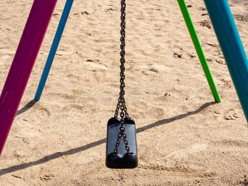 Swing on sandy children`s playground with black plastic seat hanging on chains. royalty free stock photos Swing on sandy children`s playground with black plastic seat hanging on chains. royalty free stock photos