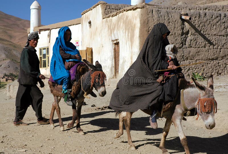 Syadara, Bamiyan Province in Afghanistan: An Afghan man walks behind two women riding donkeys in the town of Syadara near Yakawlang in Central Afghanistan. Man with women and donkeys. Syadara, Bamiyan Province in Afghanistan: An Afghan man walks behind two women riding donkeys in the town of Syadara near Yakawlang in Central Afghanistan. Man with women and donkeys