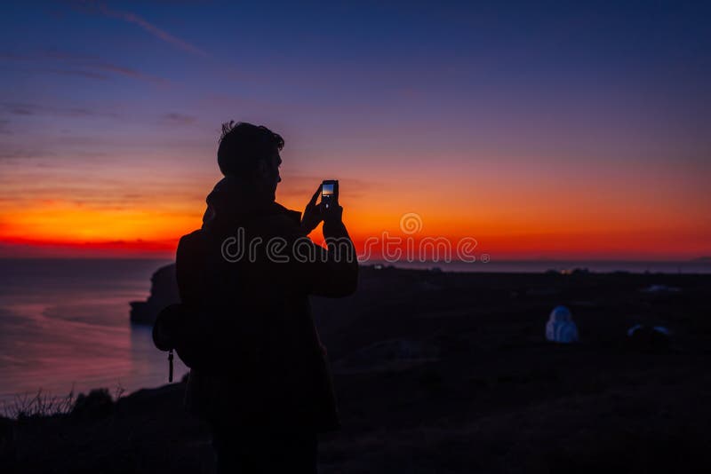 Sylwetka męska wędrująca po zachodzie słońca na wyspie Santorini Turystyczny fotograf na smartfonie zdjęcia royalty free