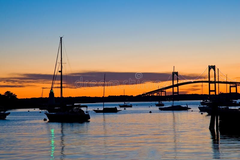 Sailboats in harbour and a high suspension bridge silhouetted against orange sunset. Newport, Rhode Island (USA). Sailboats in harbour and a high suspension bridge silhouetted against orange sunset. Newport, Rhode Island (USA)
