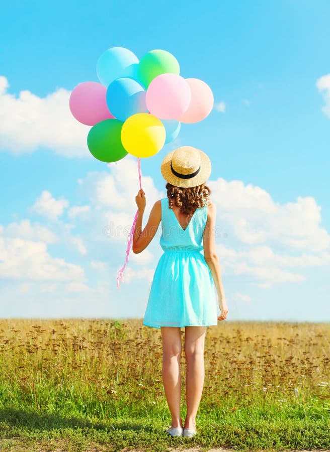 Silhouette happy woman stands with an air colorful balloons in a straw hat enjoying a summer day on a field and blue sky background. Silhouette happy woman stands with an air colorful balloons in a straw hat enjoying a summer day on a field and blue sky background