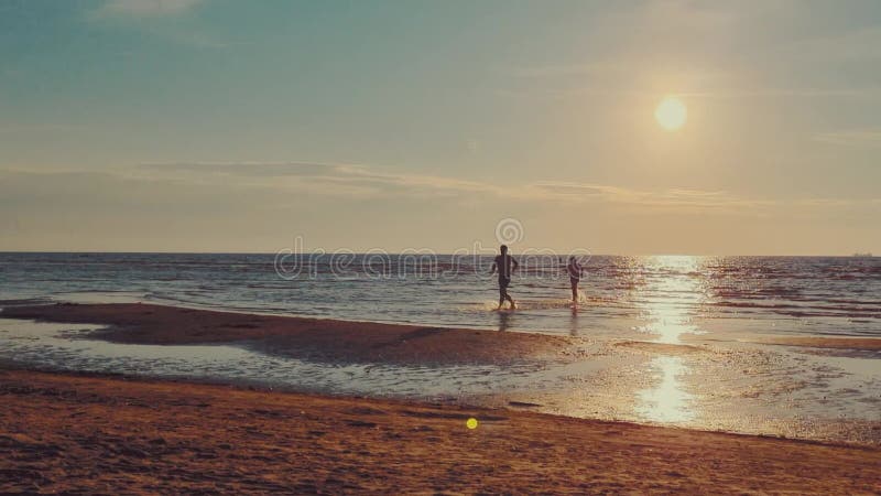 Sylwetki ludzi wypływające z morza na plaży o zachodzie słońca. zwolniony ruch