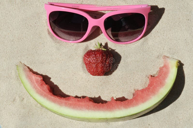 Symbolic happy summer face made out of fruit and sunglasses in the sand. Symbolic stock images, royalty-free photos and pictures