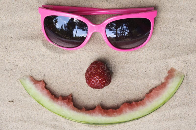 Symbolic happy summer face made out of fruit and sunglasses in the sand. Symbolic stock images, royalty-free photos and pictures