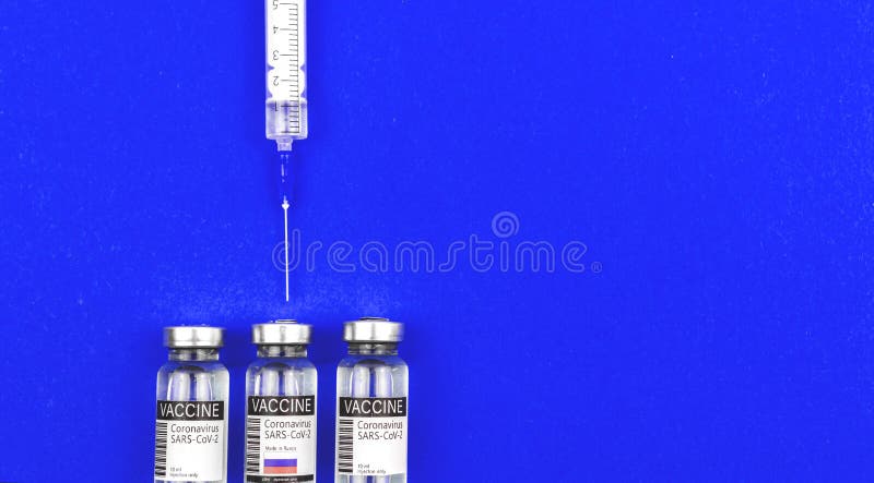 Syringe with COVID-19 vacicne, USA, UK and Russia country flags on a labels, blue background, concept of choosing