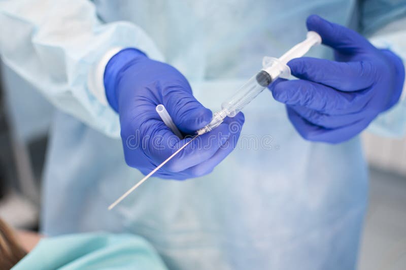 A Syringe with a Long Needle in the Hands of a Dressed Surgeon in the Operating Room Stock Photo