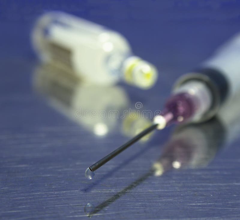 Syringe with sharp needle and droplet in shallow dof with ampule in background. Syringe with sharp needle and droplet in shallow dof with ampule in background