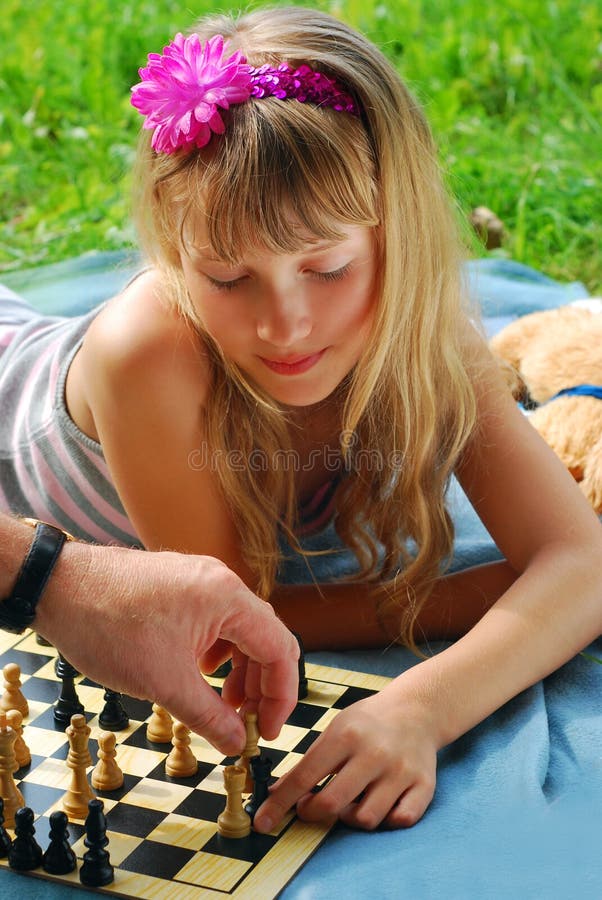 Young girl playing chess with father lying on the blanket on the picnic. Young girl playing chess with father lying on the blanket on the picnic