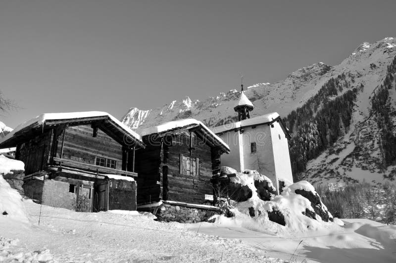 Two old wooden chalets and a chapel in the swiss mountains after a snow storm in monochrome. Two old wooden chalets and a chapel in the swiss mountains after a snow storm in monochrome