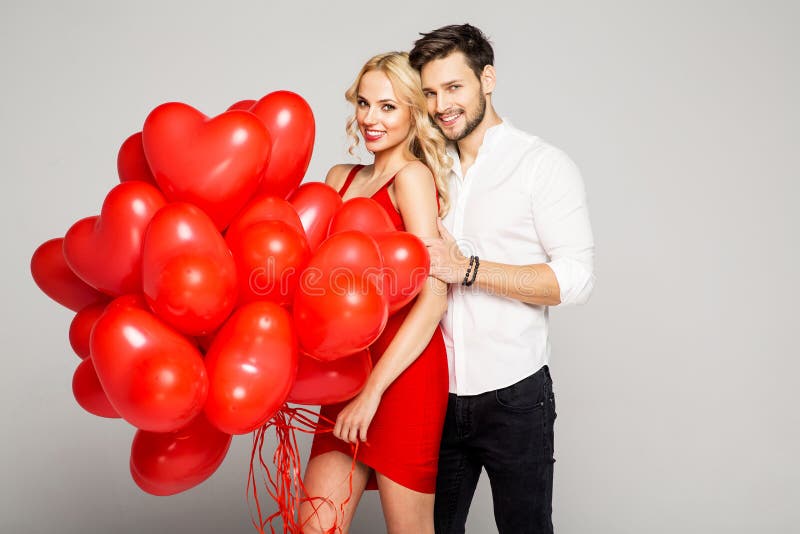 Happy beautiful couple looking at each other and holding balloons heart. Valentine`s day. Happy beautiful couple posing on grey background and holding balloons heart.