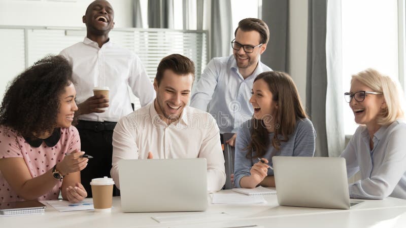 Happy cheerful diverse office workers team laughing at funny joke work together at corporate group business meeting, excited smiling employees colleagues talking having fun in workplace with laptop. Happy cheerful diverse office workers team laughing at funny joke work together at corporate group business meeting, excited smiling employees colleagues talking having fun in workplace with laptop