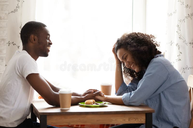 Szczęśliwy amerykanin afrykańskiego pochodzenia mężczyzna na dacie z atrakcyjną dziewczyną w kawiarni